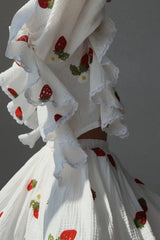 Detail shot of the ruffled sleeves and strawberry print on the white blouse and skirt.