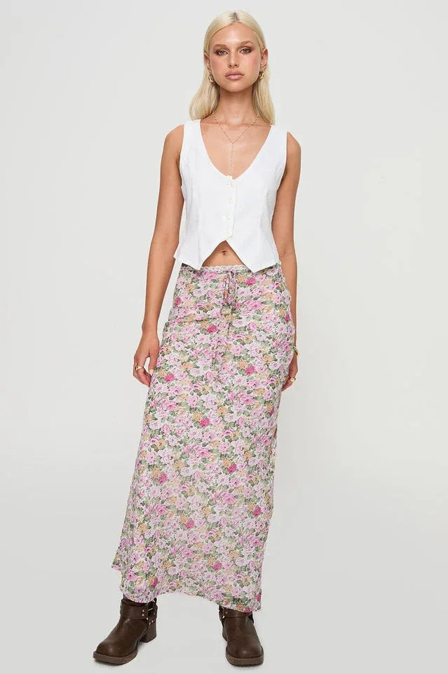 Full body shot of a woman in a white button-up vest and a floral maxi skirt.