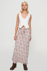 Full body shot of a woman in a white button-up vest and a floral maxi skirt.