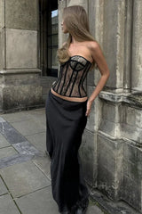 Woman wearing a black lace corset top and a black skirt, leaning against a stone pillar