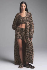 Woman wearing a leopard print fuzzy robe over a matching crop top and shorts with slippers.