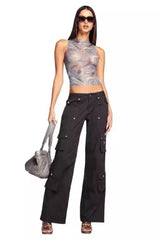 Full body shot of a woman in a marble print mesh tank top and black cargo pants holding a handbag