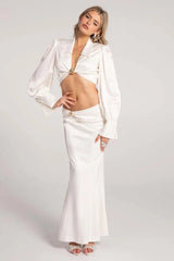 Woman in a white satin two-piece set, posing with one hand on her hip.