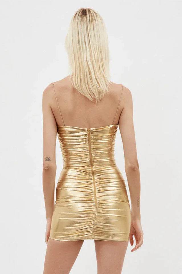 Back view of a woman in a gold metallic ruched mini dress with a sweetheart neckline and thin straps, showing zipper closure.