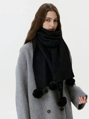 Woman wearing a black knit scarf with pom-pom embellishments