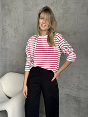 Woman wearing a white and red striped long-sleeve top and black pants, posing against a grey wall.
