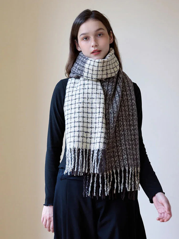 Woman wearing a black long-sleeve top and a plaid scarf with fringe detail, styled loosely around her neck.