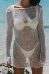 Close-up of a woman wearing a white sheer knit mini dress over a bikini on a beach.