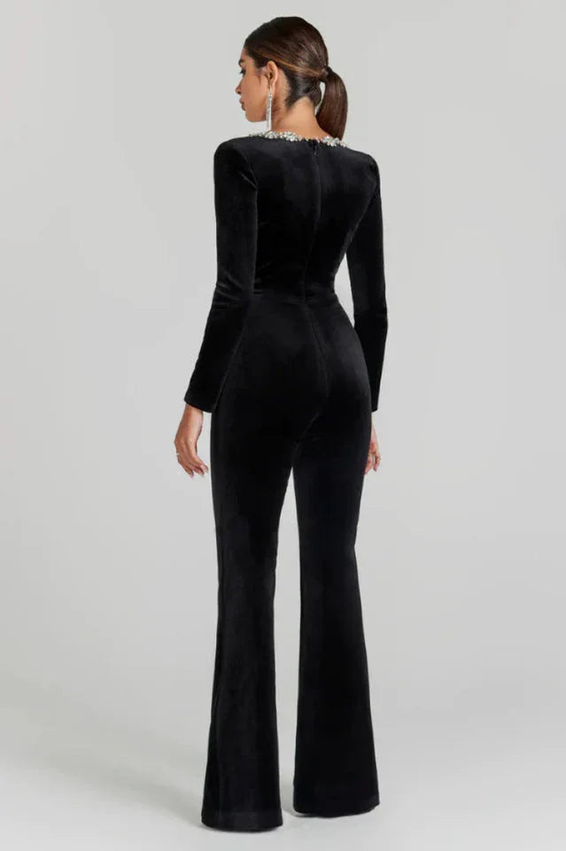 Back view of a woman in a black velvet jumpsuit with a square neckline and flared legs.
