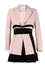 Studio product shot of a light pink blazer with a black wrap belt and black skirt, with zipper details visible.