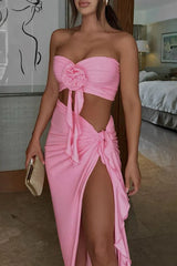 A woman is shown from the chest down, wearing a pink two-piece ensemble with a prominent thigh-high slit.