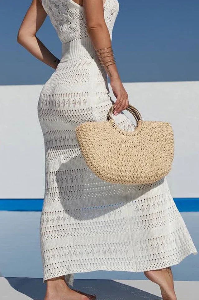 Close-up of a woman's side profile wearing a white crochet knit maxi dress and holding a straw handbag.