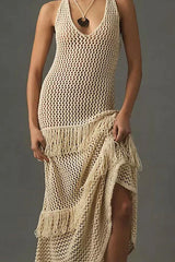 Front view close-up of a woman wearing a cream crochet knit maxi dress with fringe details, against a grey background.