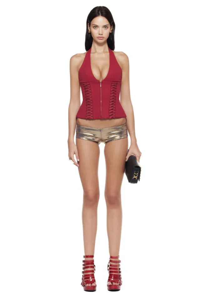 Full-body view of a model wearing a red halter corset top with gold shorts and red strappy heels.