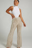Woman wearing a white sleeveless mock neck bodysuit with a cutout on the side paired with gold sequined flared pants.