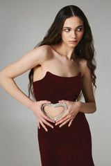 Model posing with hands near her waist, showcasing a burgundy velvet strapless mini dress with a heart-shaped cutout embellished with rhinestones.