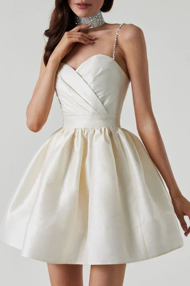 Woman wearing a short, ivory satin dress with a sweetheart neckline, embellished spaghetti straps, and a full A-line skirt.