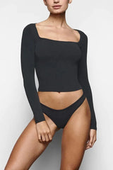 Woman wearing a black long-sleeve cropped top and matching high-cut briefs, front view.