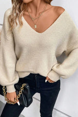 Woman wearing a cream V-neck knit sweater with lantern sleeves and black jeans, holding a black handbag