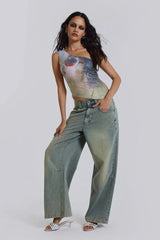 Woman posing in a one-shoulder sequined top with a graphic print and light wash wide-leg jeans.