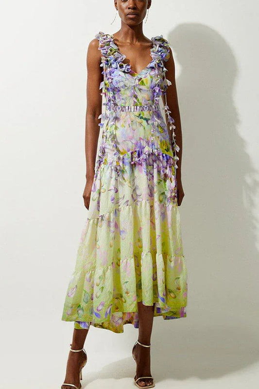 Woman wearing a pastel yellow and purple floral print midi dress with ruffled straps and tiered skirt.
