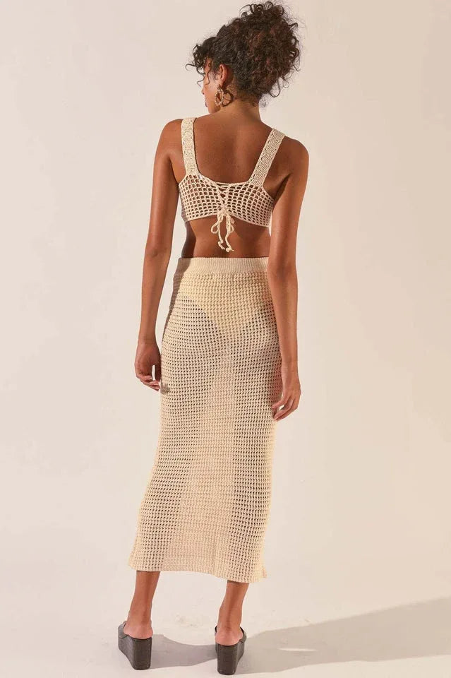 Woman wearing a cream crochet knit crop top and matching maxi skirt, back view.