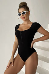 Woman wearing a black ribbed knit one-piece swimsuit with short sleeves and a zipper closure, angled view.