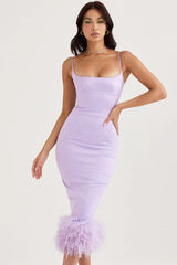 woman in a lavender midi dress with feather trim, standing with her hands on her hips