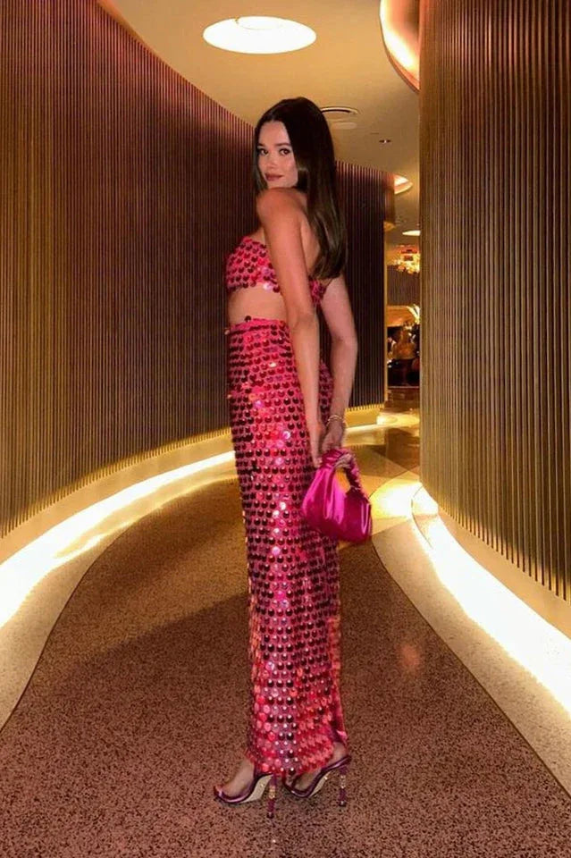 Woman wearing a pink sequined strapless top and matching full-length skirt posing in an indoor hallway, showing the side profile.