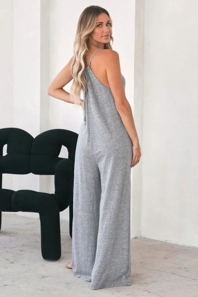 Back view of a woman in a grey wide leg jumpsuit with spaghetti straps.