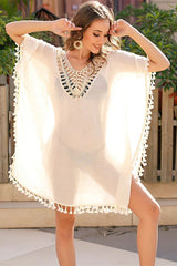 Woman posing in a white beach cover-up with tassels and crochet trim