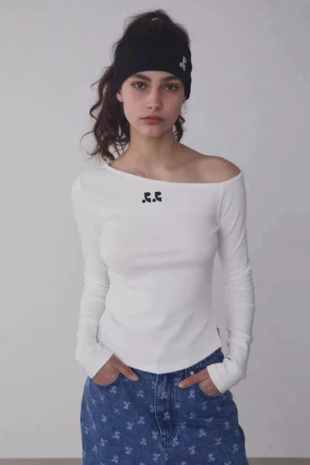 Woman wearing a white off-the-shoulder long-sleeve top with a black beanie and blue patterned jeans, front view.
