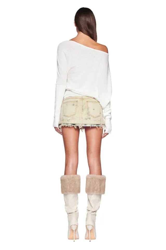 Back view of a woman wearing a white off-the-shoulder sweater and a distressed denim mini skirt, with cream boots and fur trim.