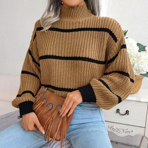 Woman wearing a brown and black striped knit sweater with a high neckline and long sleeves, holding a brown fringed purse, paired with light blue jeans.