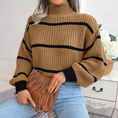 Woman wearing a brown and black striped knit sweater with a high neckline and long sleeves, holding a brown fringed purse, paired with light blue jeans.
