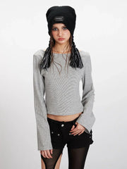 Close-up front view of a model wearing a grey and white striped long-sleeved cropped top with flared sleeves, black shorts with cut-outs, black and grey striped thigh-high socks, and black sneakers. She is also wearing a black beanie.