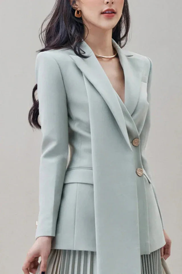 Close-up of a woman wearing a light blue blazer with a shawl lapel and two gold buttons.