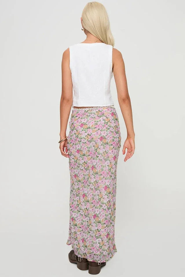 Back view of a woman in a white sleeveless vest and a floral maxi skirt.