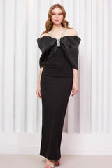 Model posing in an elegant black floor-length dress with an off-the-shoulder bow design