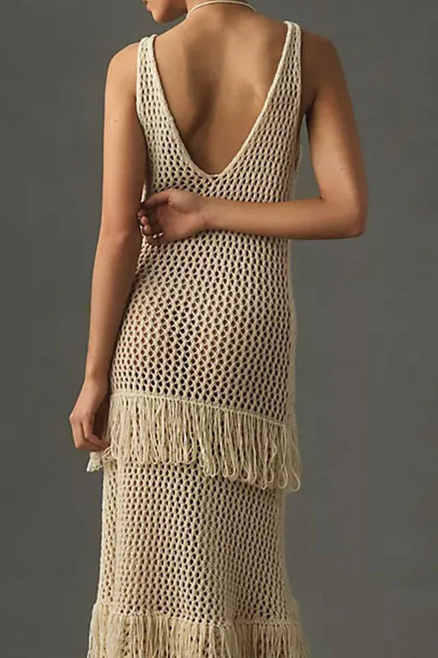Back view close-up of a woman wearing a cream crochet knit maxi dress with fringe details, against a grey background.