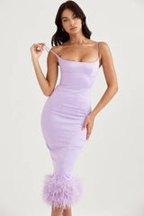 woman wearing a lavender midi dress with feather trim and spaghetti straps, posing with her hand on her hip