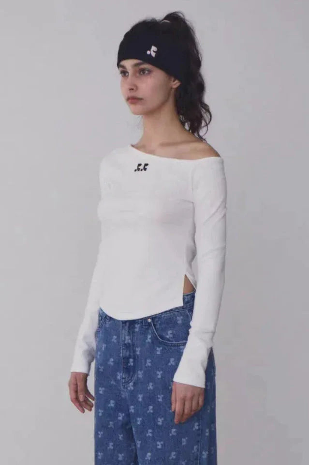 Woman wearing a white off-the-shoulder long-sleeve top with a black beanie and blue patterned jeans, side view.