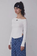 Woman wearing a white off-the-shoulder long-sleeve top with a black beanie and blue patterned jeans, side view.