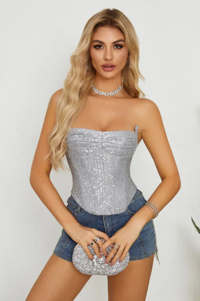 Woman wearing a silver sequined strapless corset top with denim shorts
