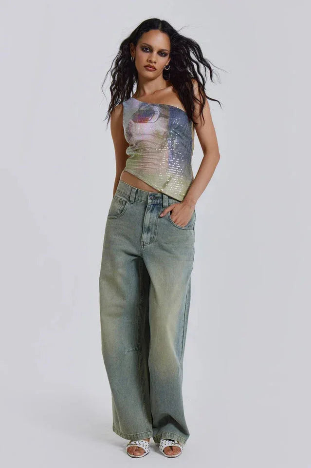 Woman wearing a one-shoulder sequined top with a graphic print and light wash wide-leg jeans.