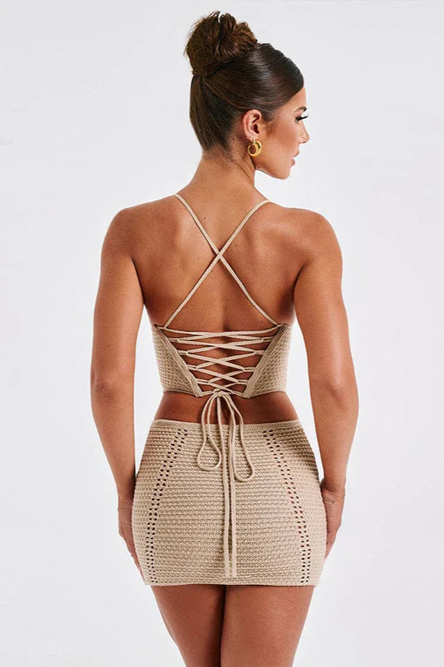 Woman wearing a beige crochet knit corset top and matching mini skirt, back view