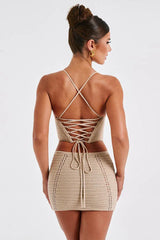 Woman wearing a beige crochet knit corset top and matching mini skirt, back view