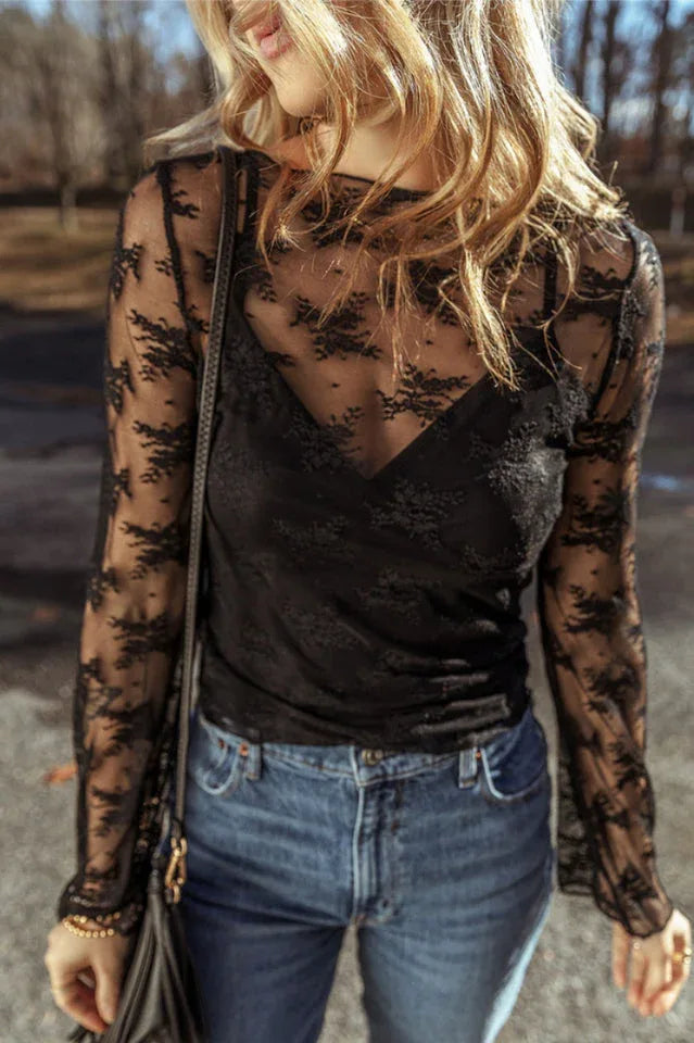 Woman wearing a black lace long-sleeved top with a scoop neckline and bell sleeves, paired with blue denim jeans.