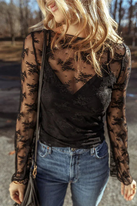 Woman wearing a black lace long-sleeved top with a scoop neckline and bell sleeves, paired with blue denim jeans.