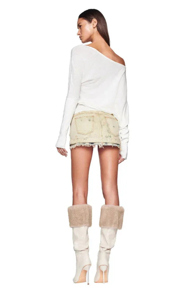 Back view of a woman wearing a white off-the-shoulder sweater and a distressed denim mini skirt, with cream boots and fur trim.